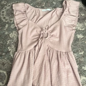 Ljusrosa topp från 157 - Säljer en söt ljusrosa topp från 157 med volangdetaljer och knytning framtill. Toppen har en ribbad struktur och korta ärmar. Har kanska använt 3 gånger! 🌸