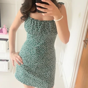 Grön blommig klänning - Söt grön kort klänning med vita blommor. Klänningen är från H&M och är i använt men fint skick!🥰