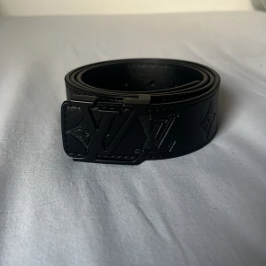 Svart bälte  - Snyggt svart bälte med präglad logotyp och stilren design. Bältet har ett matchande svart spänne . Storlek 105. Perfekt för att ge en lyxig touch till din outfit.