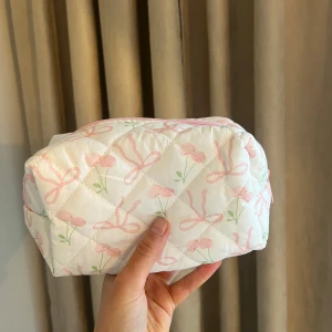 Vit quiltad necessär med rosa rosetter - Söt vit quiltad necessär med rosa rosetter och gröna detaljer. Perfekt för att förvara smink eller andra småsaker. Den har en praktisk dragkedja i rosa som håller allt säkert på plats. Säljer alla 3 men är 150kr/st 