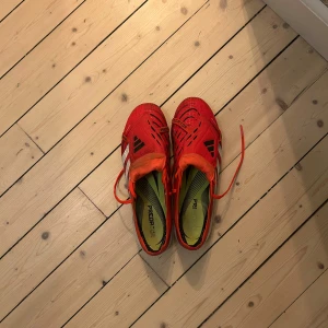 Röda fotbollsskor från Adidas - Säljer dessa predetor för har tröttnat på dom, använda några gånger men hela och fina, de svarta som syns är lite missfärgning från granulat på planen, skick är 8.5/10, det är AG dobbar 