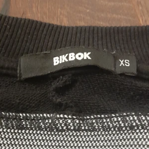 Svart tröja med vita ränder från BikBok - Säljer en svart tröja från BikBok i storlek XS. Tröjan har vita ränder längs ärmarna och ribbade muddar vid ärmslut och hals. Material är i froté, bra för träning.