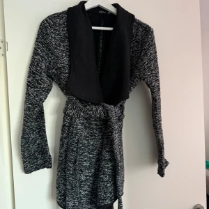 Svart och grå stickad klänning från Boohoo - Mysig svart och grå stickad klänning från Boohoo med långa ärmar och en bred krage. Perfekt för kyligare dagar med sin bekväma passform och stilrena design.