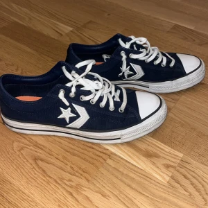 Blåa Converse All Star sneakers - Säljer ett par klassiska blåa Converse All Star sneakers med vita detaljer och snörning. Skorna har den ikoniska stjärnloggan på sidan och en vit tåhätta. Perfekta för en avslappnad stil.