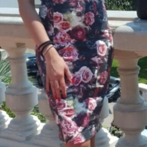 Blommig klänning med rosor - Snygg blommig klänning med ett vackert rosmönster i rosa och vita nyanser på en mörk bakgrund. Klänningen har breda axelband och en figurnära passform som framhäver silhuetten. Perfekt för en somrig dag eller en speciell kväll.