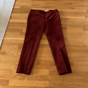 Vinröda kostymbyxor - Snygga vinröda kostymbyxor med en elegant passform. Perfekta för en stilren look. Byxorna har en klassisk design med knappar och dragkedja framtill.