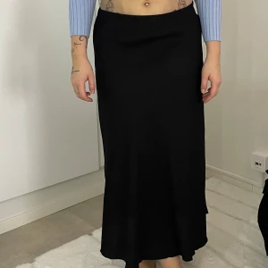 Svart långkjol - Snygg svart långkjol i ett elegant och tidlöst snitt. Kjolen har en slät yta och faller fint längs benen. Perfekt för att skapa en stilren look.