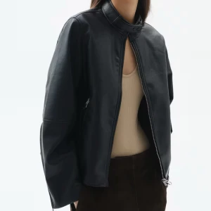 Svart skinnjacka med dragkedja - Snygg svart skinnjacka från H&M med dragkedja och rund hals. Jackan har en stilren design med långa ärmar och en kortare passform. Perfekt för en cool look.