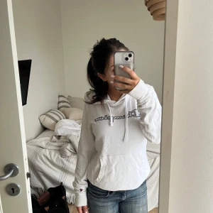 Vit hoodie från Champion - Säljer en vit hoodie från Champion med logga på bröstet. Den har en klassisk känguruficka och justerbar huva med snören. Perfekt för en avslappnad stil. Den är i storlek L men passar mig som brukar ha xs-s, konstigt jag vet.