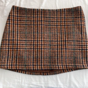 Rutig kjol i brun - Snygg rutig kortkjol i bruna nyanser. Perfekt för en stilren look med en klassisk touch. Kjolen har en enkel design utan detaljer som knappar.