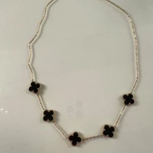 Halsband med svarta fyrklöver - Halsband med fem svarta fyrklöverformade hängen. Kedjan är i guldton och ger en lyxig känsla. Perfekt för att ge en stilren touch till din outfit.