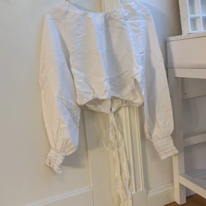 Vit blus från Kappahl - Säljer en vit blus från Kappahl i storlek XS. Blusen har långa ärmar med resår vid ärmsluten och en knytning backtill som ger en fin detalj. Ryggen är relativt öppen och tröjan är cropped. Blusen är helt ny och kostade 499 kr från början. Skriv om du har fler frågor!