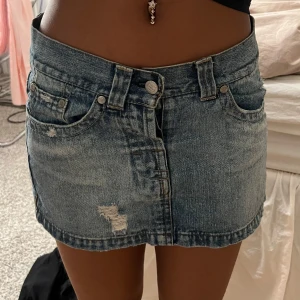 Blå jeanskjol från Abercrombie & Fitch - Trendig blå jeanskjol från Abercrombie & Fitch med slitna detaljer och klassisk femficksdesign. Perfekt för en avslappnad look. Kjolen har en kort längd och stängs med knapp!