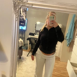 Svart hoodie från Juicy Couture - Säljer en svart hoodie från Juicy Couture med dragkedja och ett stort broderat emblem på ryggen. Hoodien har långa ärmar och är tillverkad i ett mjukt material. Perfekt för en avslappnad stil.