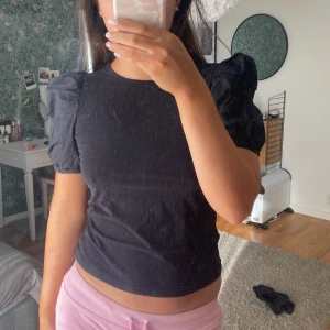 Svart topp med puffärmar - Säljer en stilren svart topp med puffiga kortärmar. Toppen har en tight passform och är perfekt för en trendig look. Den är enkel men elegant och kan lätt matchas med olika outfits.