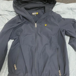  Lyle & Scott jacka  - Säljer en mörkblå jacka från Lyle & Scott i storlek 12/13 år. Jackan har en dragkedja framtill och två fickor med dragkedjor. Perfekt för kyliga dagar med sin stilrena design och praktiska detaljer.
