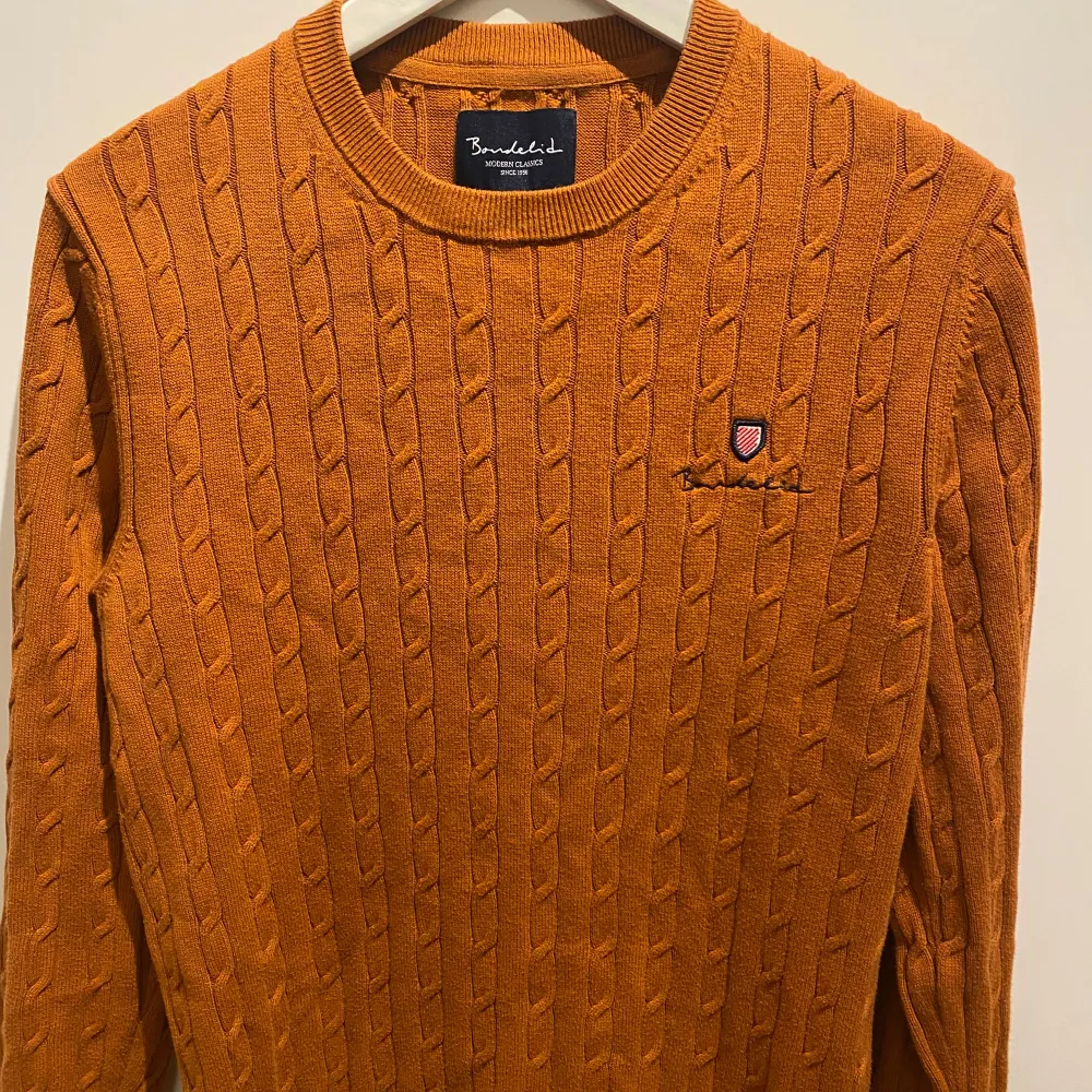 Säljer min kabelstickade Bondelidtröja som är använd, men i bra skick. Dave cable crew neck i orange färg med en liten broderad logotyp på bröstet.. Tröjor & Koftor.