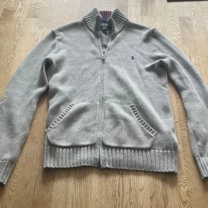 Grå Ralph-lauren zip i bomull - Storlek: 160 (14/16 år), mycket bra skick har används fåtal gånger, perfekt till hösten och vintern och väldigt bekväm! 