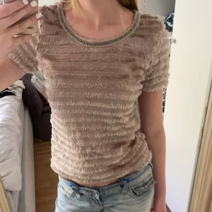 Beige kortärmad topp med textur - Säljer en superfin beige topp med korta ärmar och en unik textur. Den har en rund halsringning med en subtil glittrig kant. Perfekt för både vardag och festliga tillfällen. Passar bra till jeans för en avslappnad look! vissa fransar sitter löst och kan därför ramla av speciellt om man drar i de!