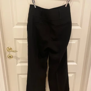 Svarta kostymbyxor från Zara - Säljer ett par stilrena svarta kostymbyxor från Zara. De är högmidjade och har en klassisk rak passform som passar perfekt för både jobb och fest. Byxorna är i nyskick och har en snygg slitsdetalj baktill. Perfekta för höst och vinter!