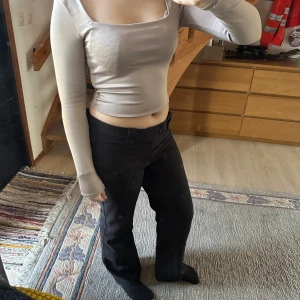 Beige långärmad topp - Säljer en stilren beige långärmad topp med tight passform. Toppen har en fyrkantig halsringning och är croppad, vilket ger en modern look. Perfekt för att matcha med både jeans och kjol.