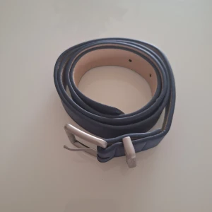 bälte - Snyggt blått bälte med ett stilrent silverfärgat spänne. Bältet har en slät yta och flera justerbara hål för perfekt passform. Perfekt för att ge din outfit en extra touch.