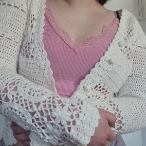 Vit virkad kofta - Charmig vit virkad kofta med vackra detaljer och blommönster. Koftan har långa ärmar och en öppen design framtill. Perfekt för att lägga till en bohemisk touch till din outfit.