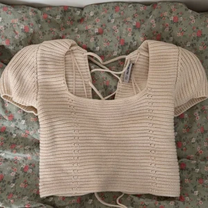 Beige stickad topp  - Säljer en beige stickad topp från Ciquelle  med korta puffärmar och snygg snörning i ryggen. Perfekt för en stilren och trendig look. Toppen är croppad och har en fyrkantig halsringning.🌸🫶🏼 Den är i storlek XS och så fin till sommaren!! Säljer pga att det inte kommer till användning..