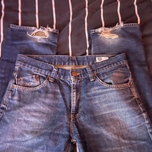 Blå jeans från Crocker - Snygga blå jeans från Crocker med slitna detaljer vid knäna. Klassisk femficksdesign och knappgylf. Perfekta för en avslappnad stil.