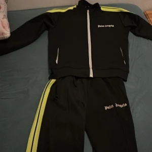 Svart träningsjacka från Palm Angels - Säljer en svart track suit från Palm Angels med vita dragkedjor och gula ränder längs ärmarna. Köpte dessa på rabbat i kicks& stuff för 4000kr. Cond 9/10. Säljer byxerna för 800kr och tröjan för 1200kr båda för 1500kr. Dom är storlek M men passar även s