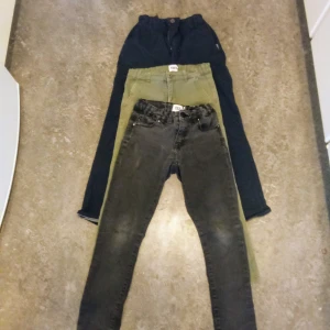 Tre par byxor i olika färger och olika tyg str140 - Säljer tre par byxor i olika färger. Ett par blåa ett par grå jeans och ett par gröna byxor. Perfekta för olika tillfällen och stilar kommer från djur och rökfritt hem . 