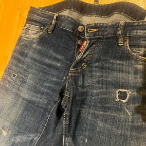 Mörkblå jeans från Dsquared2 - Snygga mörkblå jeans från Dsquared2 med slitna detaljer och en klassisk femficksdesign. Jeansen har en knappgylf och är perfekta för en avslappnad stil. Märkeslogga synlig vid fickan.