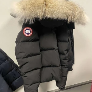 Canada gosse  - Säljer en svart dunjacka från Canada Goose med en lyxig pälsdetalj på huvan. Jackan har en klassisk design med en rund logotyp på bröstet och är perfekt för kalla vinterdagar. Den är både stilren och funktionell.