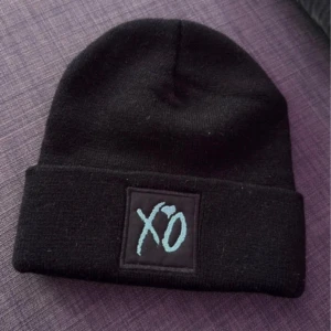 Svart mössa med XO och Starboy broderi - Snygg svart mössa med XO broderat i ljusblått på ena sidan och 'Starboy Legend of the Fall' i rött på andra sidan. Perfekt för att hålla sig varm och stilren under kyliga dagar. LIMITED EDITION