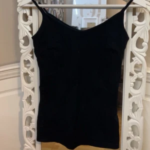 Svart linnetopp från 157 - Säljer en stilren svart linnetopp från 157. Toppen har smala axelband och är tillverkad i en mjuk bomullsblandning med elastan för extra komfort. Perfekt för lager-på-lager eller att bära som den är.