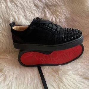 Svarta snygga Christian Louboutin skor  - Snygga svarta christian Louboutin nitar på ovansidan och en ikonisk röd sula. Skorna har snörning och är tillverkade i ett material som liknar mocka. Perfekta för att ge din outfit en edgy touch.