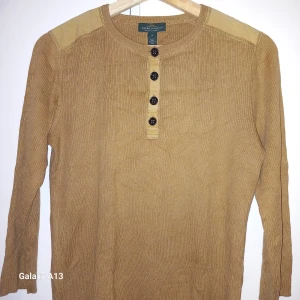 Beige ribbad tröja från Ralph Lauren - Säljer en snygg beige ribbad tröja från Ralph Lauren. Tröjan har långa ärmar och knappar framtill. Perfekt för en stilren look. Passar bra till både jeans och chinos.