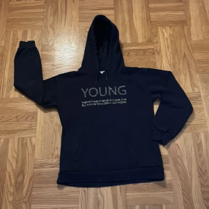 Svart hoodie med text från Gina Tricot - Säljer en svart hoodie från Gina Tricot med texten 'YOUNG' i glittriga stenar på framsidan💗Tröjan har en klassisk känguruficka och en bekväm huva💗Den är i gott skick💗Perfekt för en avslappnad stil💗Säljer den för 75 kr 💗Vid intresse av tröjan hör av er💗💗