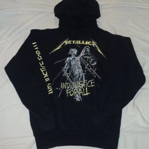 Svart Metallica hoodie - Säljer en svart hoodie med Metallica-tryck och texten '...And Justice For All'. Tröjan har en klassisk hoodie-design med långa ärmar och en stor ficka framtill. Perfekt för fans av bandet!