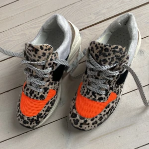 Leopardmönstrade sneakers med orange detaljer - Vårens glädjepjuck med zebra- och leopardmönstrat pälstyg och neon orange. Chunky sula med en svart fläck. (syns på bild) Kanske inte de mest ergonomiska dojjerna i stan men istället desto mer attityd. 