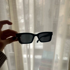 Svarta rektangulära solglasögon - Snygga svarta solglasögon med rektangulära bågar. Perfekta för en stilren look. De har en liten gulddetalj på sidan av skalmen som ger en extra touch av elegans.