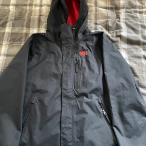 Helly Hansen skidjacka  - Svart skidjacka från Helly Hansen med röda detaljer. Använd under en vecka i fjällen så väldigt bra skick. Strl L. Nypris 3999 kr. 