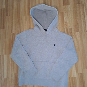 Grå hoodie från Ralph Lauren - Säljer en stilren grå hoodie från Ralph Lauren med det klassiska broderade logotypen på bröstet. Tröjan har en bekväm passform och en stor huva. Perfekt för en avslappnad look. 9/10 skick