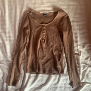 Brun långärmad topp från Gina Tricot - Säljer en brun långärmad topp från Gina Tricot med knappar framtill. Perfekt för en avslappnad stil och passar bra till jeans eller kjol. Toppen har en rund halsringning och är gjord i ett mjukt material. kan säljas tillsammans med den blåa för ett lägre paketpris! storlek m men passar även s.