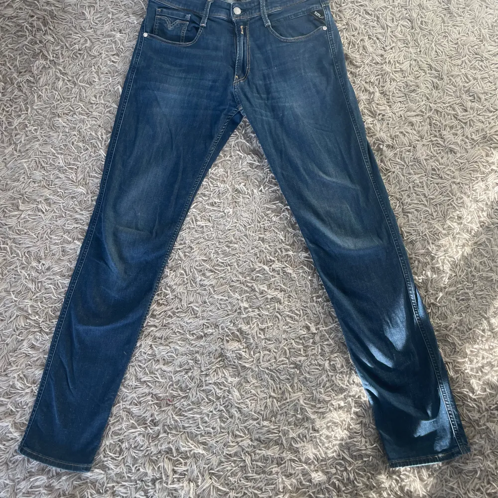 Snygga blå jeans från Replay med klassisk femficksdesign och snygga sömmar på bakfickorna. De har en knappgylf och är perfekta för en avslappnad stil. Märkeslappen i läder på baksidan ger en extra touch.. Farkut & Housut.