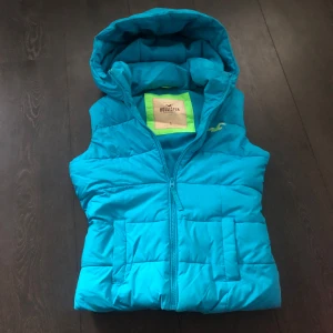 Turkos dunväst från Hollister - Snygg turkos dunväst från Hollister med huva och dragkedja. Mjuk å varm insida, värmer mer än vad man kan tro 🥰