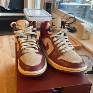 Nike Air Jordans i röd och beige - Snygga Nike Air Jordans i röd och beige med unikt mönster på hälen. Skorna har snörning och en klassisk Air Jordan-logga på sidan. Perfekta för den som vill sticka ut med stil.