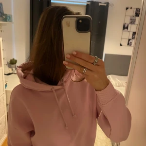 Rosa hoodie - Säljer en mysig rosa hoodie med justerbar dragsko i huvan. Perfekt för en avslappnad stil och passar bra till jeans eller leggings. Den har långa ärmar och ribbade muddar vid ärmslut och nederkant.