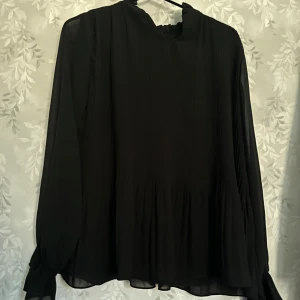 Svart NA-KD blus - Säljer nu min fina NA-KD blus som tyvärr inte har kommit till andvändning, denna är max andvänd 2 gånger och är inprincip i ny skick. Den har ett typ av ”räffel” på framsidan och baksidan vilket är  snyggt. Den är även sann i storleken❤️ skriv för frågor eller funderingar🥰