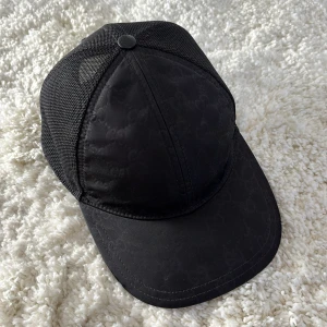 Gucci Nylon Baseball Keps - Svart - Snygg svart keps från Gucci med diskret mönster och meshdetaljer. Kepsen har en justerbar rem baktill för perfekt passform. Perfekt för en stilren look. Det enda som är negativt är att spännet ibak  är lite trasigt (kolla sista bilden) men det går fortfarande att använda bara man är försiktig. Annars fint skick. Kepsen köptes hos kicksnstuff i Göteborg så den är såklart äkta.